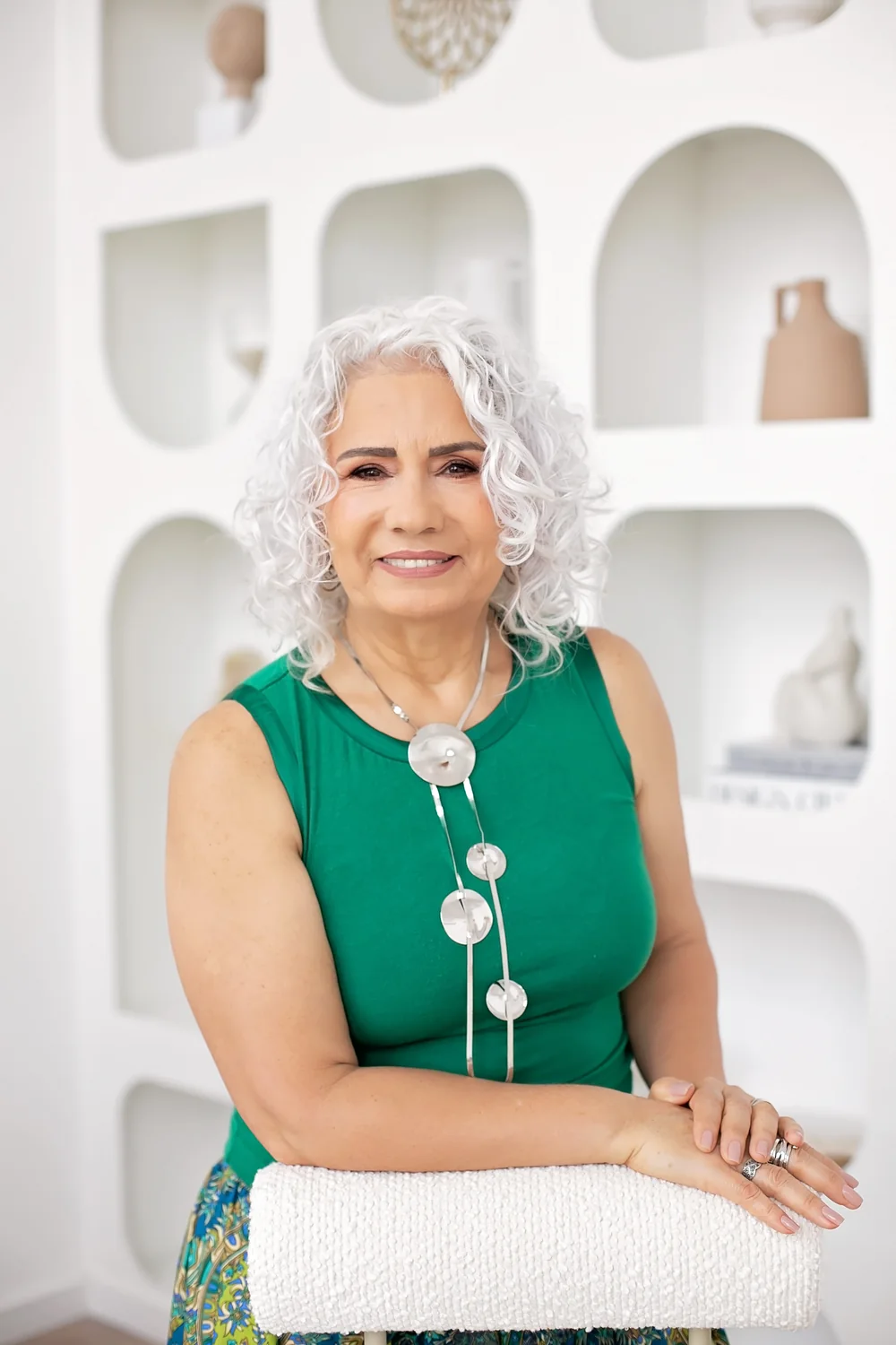 Madalena Borges sorrindo, com blusa verde e as mãos apoiadas em uma cadeira