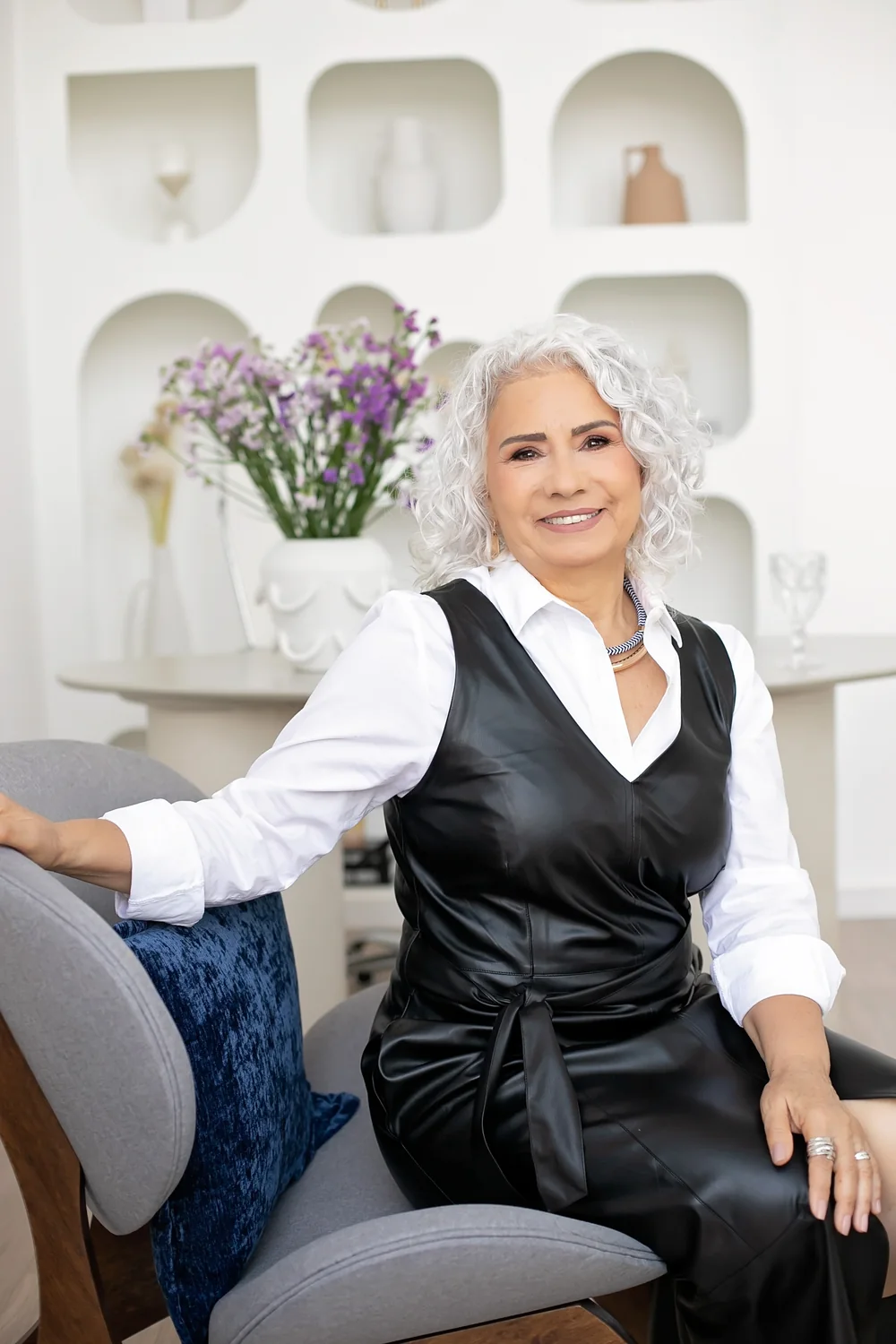 Madalena Borges sorrindo, sentada em uma poltrona, com camisa branca