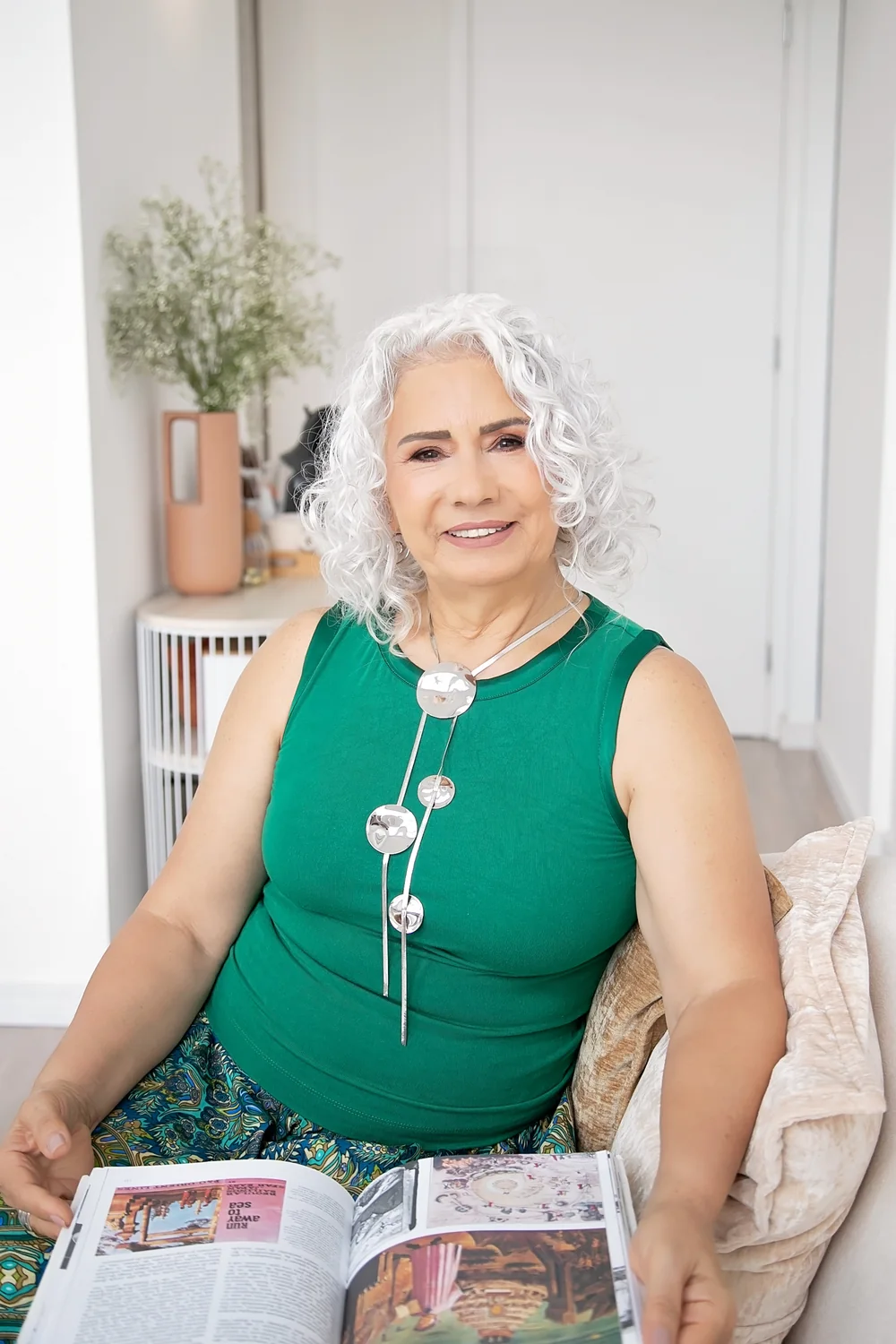 Madalena Borges sorrindo, sentada em um sofá, com um livro aberto